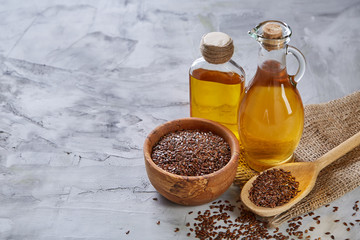 Flax seeds in bowl and flaxseed oil in glass bottle on light textured background, top view,...