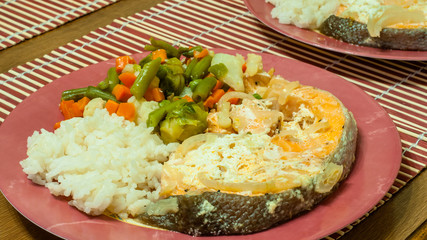 baked red fish with rice and vegetables in a ceramic dish on a table. close-up