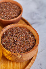 Flax seeds in bowl and flaxseed oil in glass bottle on light textured background, top view, close-up, selective focus