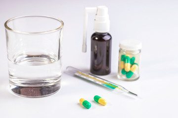 Tablets, a glass of pure water, a thermometer. On a white background.