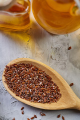 Flax seeds in bowl and flaxseed oil in glass bottle on light textured background, top view, close-up, selective focus