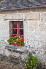 Fototapeta na wymiar Red window with flowers on windowsill and old medieval decorative wall