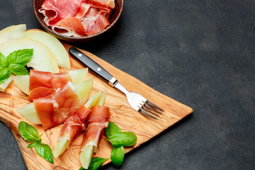 italian food with melon and prosciutto on wooden cutting board