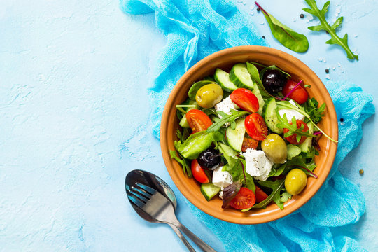 Greek salad with fresh vegetables, feta cheese and black olives on a blue stone or concrete table. Copy space, top view flat lay background.