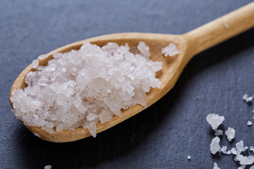 Crystal sea salt in a wooden spoon on dark background, top view, close-up, selective focus.