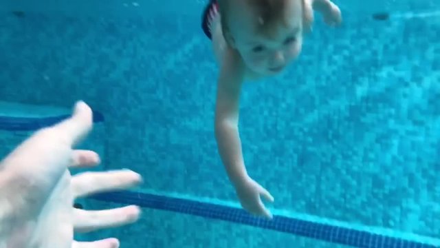 Happy baby boy diving under the water in the swimming pool. An underwater shot