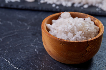 Large white sea salt in a natural wooden bowl on white background, top view, close-up, selective focus