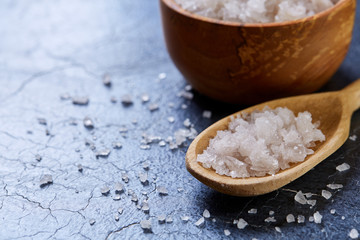 Crystal sea salt in a wooden spoon on dark background, top view, close-up, selective focus.