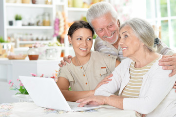 happy senior couple with adult daughter using laptop 
