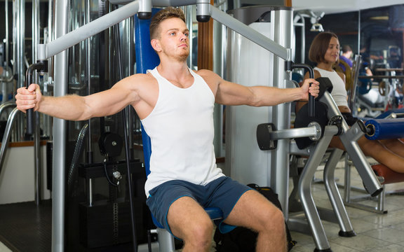 well trained man using pec deck gym machinery indoors