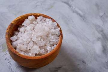 Large white sea salt in a natural wooden bowl on white background, top view, close-up, selective focus