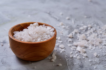 Large white sea salt in a natural wooden bowl on white background, top view, close-up, selective focus