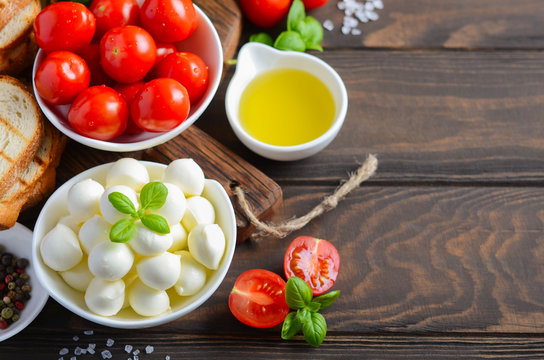 Italian food ingredients – mozzarella, tomatoes, basil and olive oil on rustic wooden table.