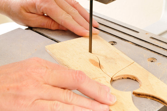 Closeup of a womans hands working with a bandsaw to cut an intricate shape in a piece of plywood