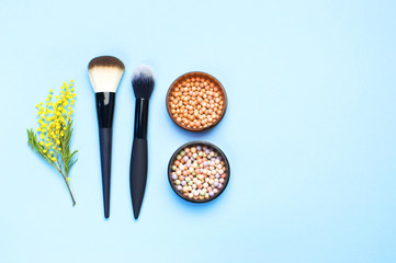 Set of decorative cosmetics for make-up Powder Rouge Corrector Brushes and flowers of mimosa on blue background. Makeup Accessories Top view Flat Lay