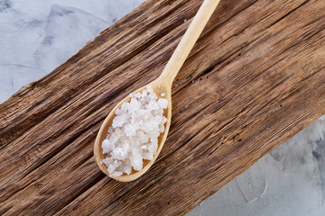 Crystal sea salt in a wooden spoon on dark vintage wooden background, top view, close-up, selective focus.