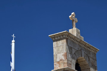 Fototapeta premium Stone Cross On The Gate and small metal cross. Stone cross on brick gate and a small metal rod with a cross on Greek flag. Greek flag is wrapped Access to the yard of the Greek Orthodox Church