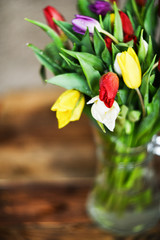 Flower background: bouquet of colorful tulips in a glass vase on a natural wooden background, postcard, mocap for mother's day greetings, international women's day