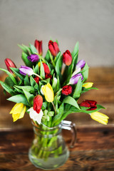 Flower background: bouquet of colorful tulips in a glass vase on a natural wooden background, postcard, mocap for mother's day greetings, international women's day