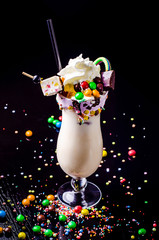 Crazy freakshake food trend. Delicious extreme milkshake with ice cream, chocolate, jam, candies, marmalade and marshmallow over black background. Happy Birthday holiday.