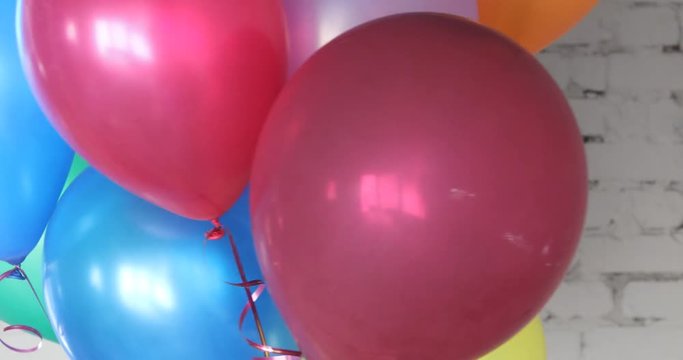 Bunch of colorful helium balloons on a bricky white wall background