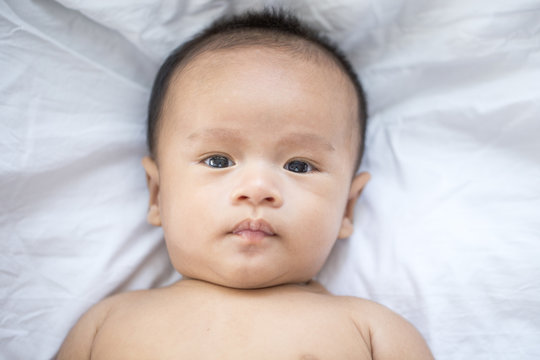 Asian newborn baby looking to camera in bed.