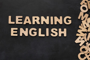Fototapeta premium Learning English spelled with wooden letters on black background