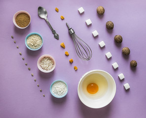 on a lilac background food knolling diagonal walnut greek seeds sunflower sugar cube refined corn spoon egg in a round bowl cake mold flour blue pink