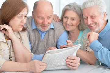 two senior couples reading newspaper