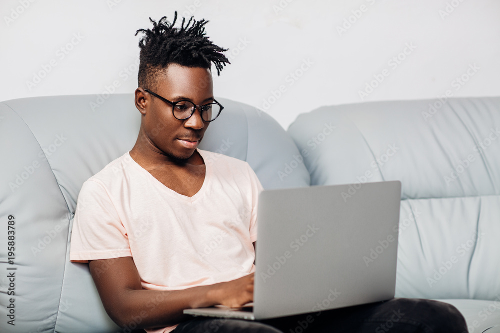 Wall mural African American man sitting with laptop on sofa