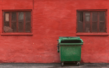 Fototapeta na wymiar green garbage container on a red wall background