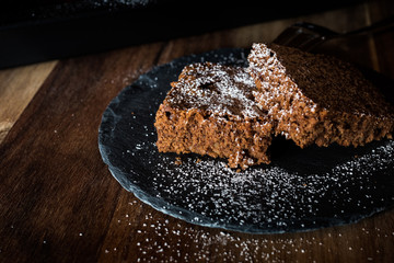Saftiger Kuchen aus Zartbitterschokolade mit Mandeln vom Blech angerichtet auf einer Schieferplatte dekoriert mit Puderzucker