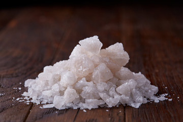 Pile of salt crystals on the dark wooden background, top view, flat lay, shallow depth of field