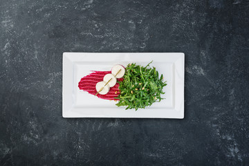 Salad - bakes beetroot slices, goat cheese, fresh arugula and pine nuts, served on the white plate.