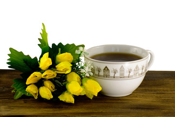 Cup of tea and yellow tulips on a wooden board. A bouquet of yellow tulips and a cup of coffee.