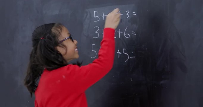 Cute female elementary school student thinking before solving a math problem on the blackboard in the classroom. Shot in 4k resolution