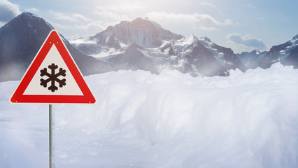 verschneite Straße im Gebirge mit rotem Warnschild