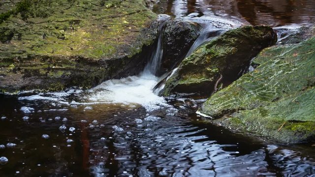 Tro Maret River in the Ardennes in East Belgium with brown  water running between green rocks forming bubbles.