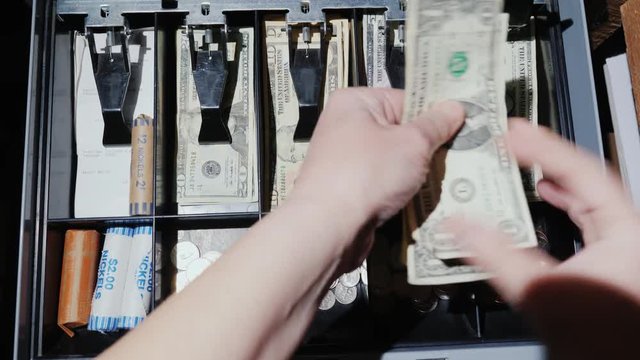 A woman cashier works with the cashier. He puts money and takes the change. Trading for cash