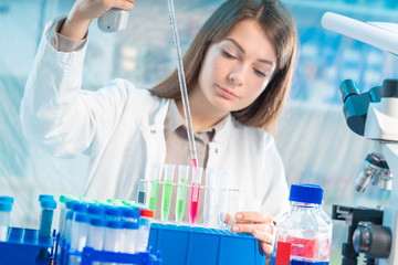 Fototapeta premium Young woman in scientific lab with pipette and chemicals in test tubes