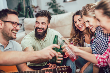 Group of happy young friends having fun and drinking beer in home interior