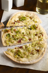 Homemade leek and bacon tarte flambee, a traditional French and German oven baked pizza-like pie, photographed with natural light (Selective Focus on the front of the middle slice)