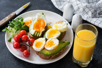 Avocado and poached egg toasts, salad and orange juice on stone table. Closeup view