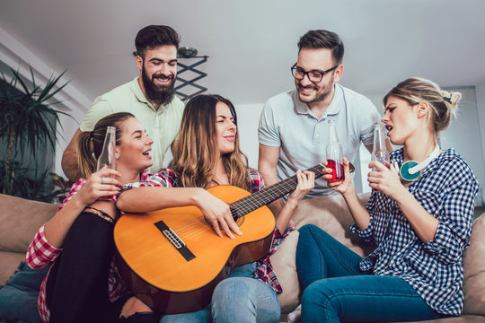 Group of happy young friends having fun and drinking beer in home interior