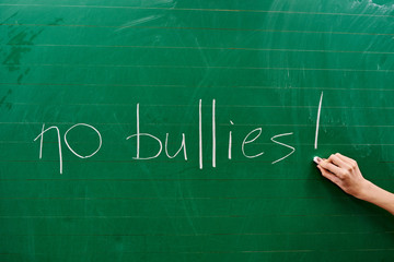 Hand of a young girl writing the words NO BULLIES on the green school board
