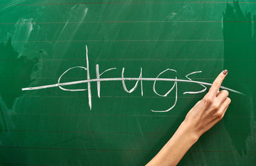 Right hand of a teenage girl writing drug protest on the green school board