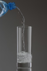 Pouring water into glass on gray background