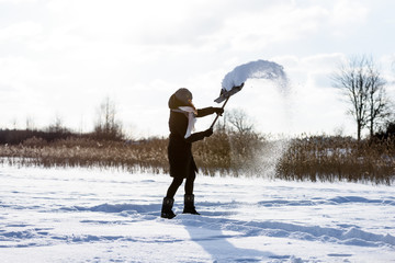 young woman in black coat cleaning ice from snow. throwing snow in the air