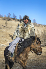 mongolian man wearing a wolf skin jacket, riding his horse in a steppe