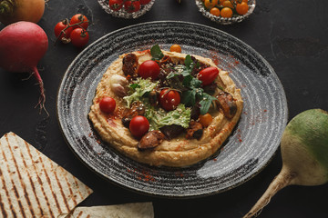 Hummus with vegetables and seafood on black background
